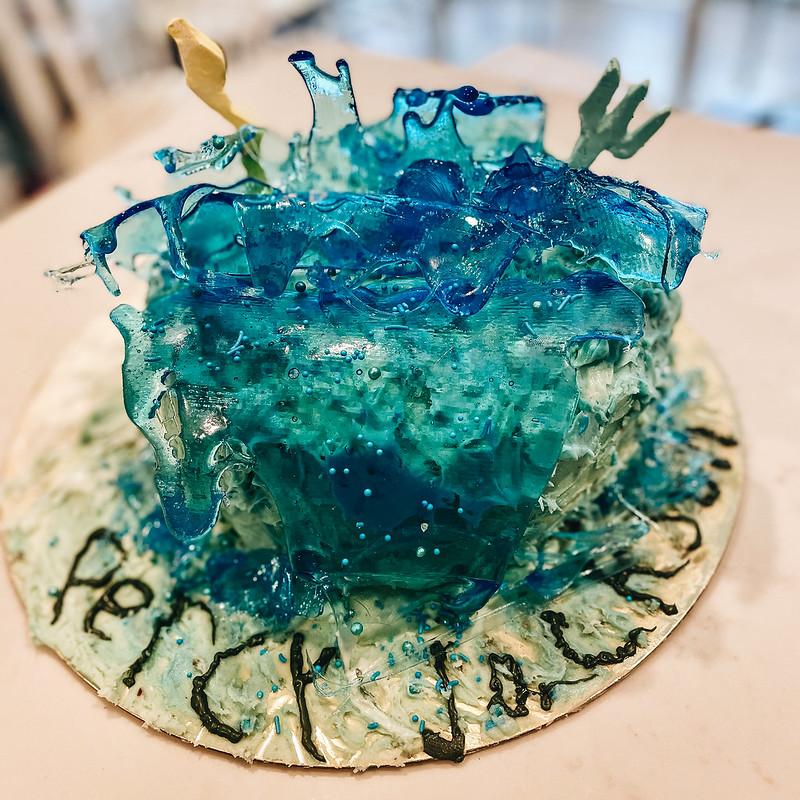 A cake decorated with blue candy waves, a lightning bolt, a trident, and icing writing Percy Jackson.